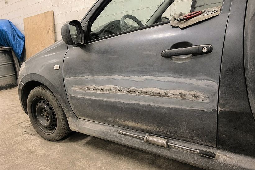 Дверь серой Lada Granta с вытянутой вмятиной, вдоль зачищенной полосы металла приварен ряд маленьких шайб, ниже лежит обратный молоток